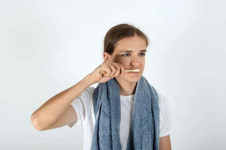 Handsome young man with terry grey bath towel over his neck is brushing his teeth. Morning routine of washing the teeth.の写真素材