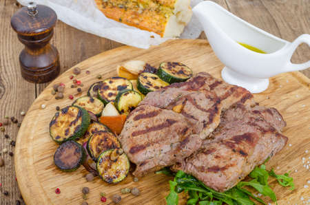 Grilled juicy barbecue steaks with fried marrow on a wooden round board. Prepared fresh food for breakfast, lunch or dinner. Lots of meat energy for good nutrition.の写真素材