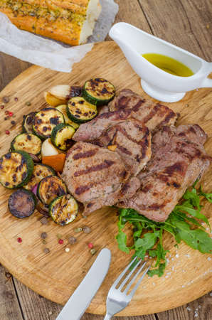Grilled juicy barbecue steaks with fried marrow on a wooden round board. Prepared fresh food for breakfast, lunch or dinner. Lots of meat energy for good nutrition.の写真素材