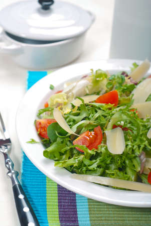 Salad of lettuce, arugula, fresh tomatoes and cheese. Delicious dish for food in a plate on the kitchen table. Delicious and fresh vegetables for a healthy diet for the whole family.の写真素材