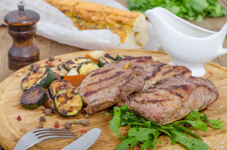 Grilled juicy barbecue steaks with fried marrow on a wooden round board. Prepared fresh food for breakfast, lunch or dinner. Lots of meat energy for good nutrition.の写真素材