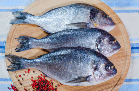 Group of raw fish prepared for cooking on cutting board at wooden table. Healthy seafood that gives a lot of energy at home. Delicious family breakfasts, lunches and dinners.の写真素材
