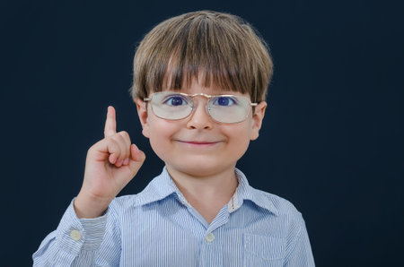 Little boy in glasses with finger up looking at camera. Smart and tidy child on training in a...