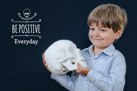 Little boy holding a skull and looking away. Smart and tidy child on training in a striped shirt....