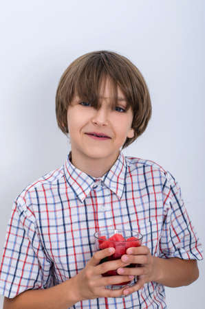 Teenage boy in a plaid shirt holding a glass of watermelon with two hands. Useful berries and fruits for children of any age. Happy children drink vitamin smoothies in summer.の写真素材