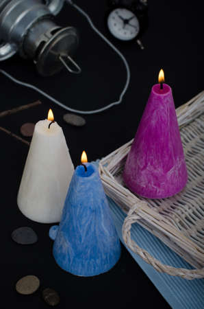Three burning candles on dark background. Melted wax candles with elegant conic original form burning at holiday table. Festive mood and atmosphere.の写真素材