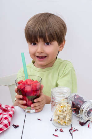 The cute boy in light green t-shirt holds a glass with watermelon cocktail and cocktail tube. Useful berries and fruits for children of any age. Happy children drink vitamin smoothies in summer.の写真素材