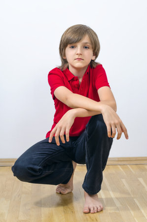 Portrait of cute kid sitting and putting hands on knee. A smart and neat child emotionally poses in a red t-shirt. Handsome and attractive boy at the studio shots.の写真素材