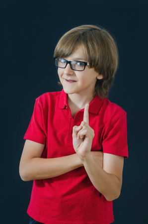 Teenager pointing a finger up and smile. Smart and tidy child on training in a red t-shirt. Quality childhood education for serious kids.の写真素材