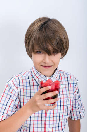 Teenage boy in a plaid shirt tries to drink a glass of watermelon slices. Useful berries and fruits for children of any age. Happy children drink vitamin smoothies in summer.の写真素材