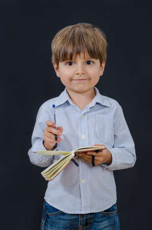 Little boy holding a notepad and looking straight ahead. Smart and tidy child on training in a striped shirt. Early childhood education for serious kids.の写真素材