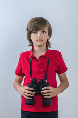 Kid with binoculars around your neck. A smart and neat child poses in a red t-shirt. A handsome and attractive boy explores and looks at the world.の写真素材