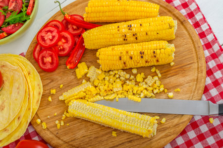 Hot grilled barbecue corn with juicy sliced tomatoes serving on a wooden round cutting board. Prepared fresh food for breakfast, lunch or dinner. Lots of meat energy for good nutrition.の写真素材