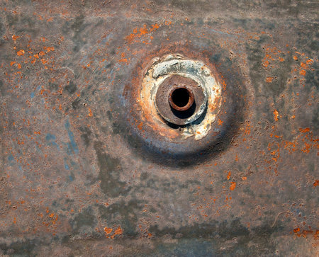 Unpainted metal texture with orifice is a complex and intriguing sight. Metal is weathered and corroded, with flakes of rust peeling off. Contrast between rough, pitted metal and orifice is striking.の写真素材