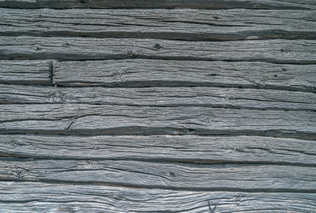 The gray vintage wooden wall of an ancient house, made from sturdy logs weathered by time. Each log, etched with the marks of seasons past, forms a mosaic of textures.の写真素材