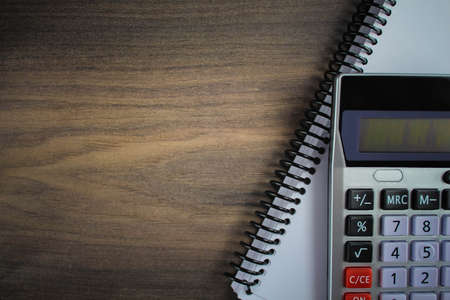 Calculator on the spiral notepad paper on the wooden background.の写真素材