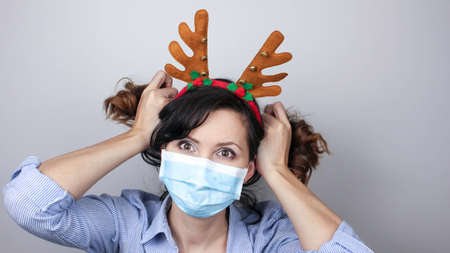 Woman wearing protection face mask against virus. Woman in a mask and deer horns headband. Funny Christmas accessory. Medical maskの写真素材