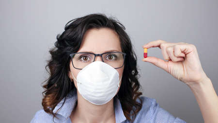 Woman wearing protection face mask against virus and glasses. Woman in a mask showing medicine pill, vaccine. Medical maskの写真素材