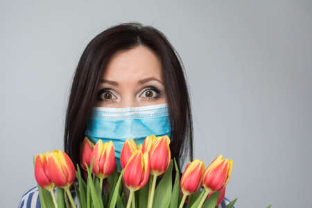 Smiling woman doctor nurse with protective medical mask, with bouquet of tulip flowers, gift, celebration, medical worker day. Mothers day. Light grey background, copy spaceの写真素材