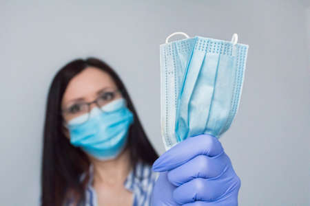 Woman wearing protection face mask against coronavirus and glasses. Woman in a mask holding medical mask on foreground. Medical mask, Close up shot, Select focusの写真素材