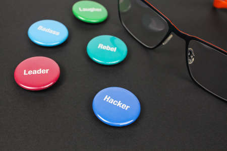 Colored plastic magnetic buttons on a black background next to glasses. Side view. Buttons with words leader, hacker, rebel, badass.の写真素材