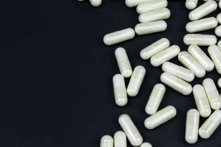 Heap of white medication and pills, capsules on black background. Top view, flat lay. Close-up.の写真素材