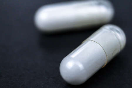 Macro view of white medication and pills, capsules on black background. Top view, flat lay. Close-up.の写真素材