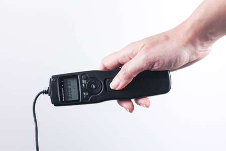 Hand holding remote control shutter switch of DSLR mirrorless camera on white background.の写真素材