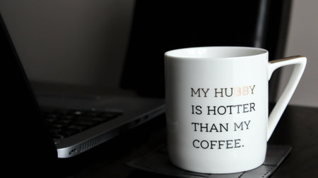 White cup with inspirational words standing next to laptop on wooden table indoorsの写真素材
