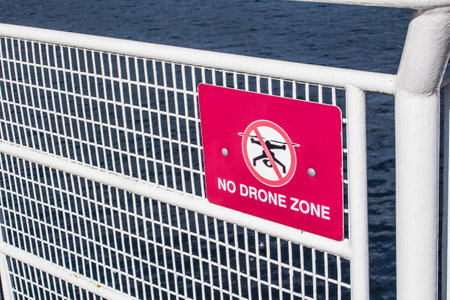 Red sign No drone allowed sign posted on a white fence. Restricted area for flying a drone. Red No drone zone sign.の写真素材