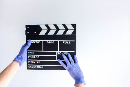 Woman in blue disposable rubber gloves holding movie clapper. Influence of pandemic on cinematographyの写真素材