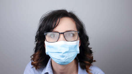 Woman wearing protection face mask against coronavirus and misted glasses. Woman in a mask looking in a mirror. Medical mask, Close up shot, Select focus, Prevention from covid19の写真素材