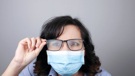 Woman wearing protection face mask against coronavirus and misted glasses. Woman in a mask looking in a mirror. Medical mask, Close up shot, Select focus, Prevention from covid19の写真素材