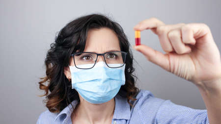 Woman in a mask showing medicine pill, vaccine. Medical mask, Close up shot, Select focus, Prevention from covid19の写真素材