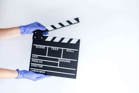 Woman in blue disposable rubber gloves holding movie clapper. Influence of pandemic on cinematographyの写真素材