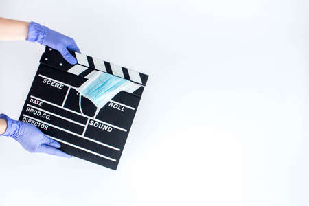 Woman in blue disposable rubber gloves holding movie clapper. Influence of pandemic on cinematographyの写真素材