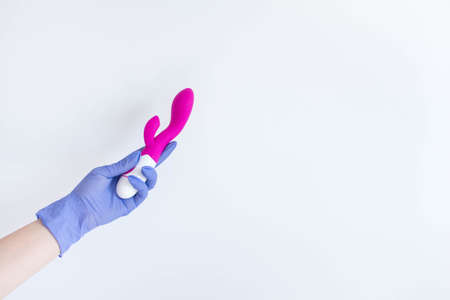 Woman's hand in latex glove holding a pink sex toy - vibrator, isolated on white backgroundの写真素材
