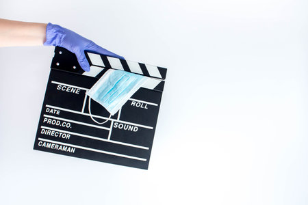 Woman in blue disposable rubber gloves holding movie clapper. Influence of pandemic on cinematographyの写真素材