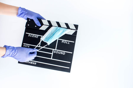 Woman in blue disposable rubber gloves holding movie clapper. Influence of pandemic on cinematographyの写真素材