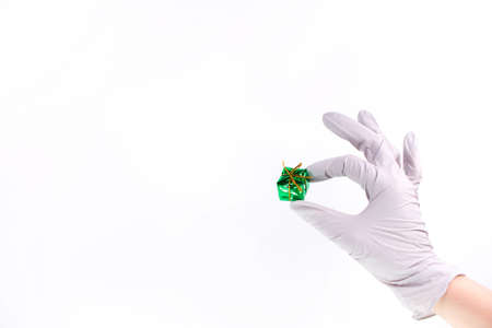 Hand with grey rubber gloves holding small green gift box with ribbon and bow for special occasion on white backgroundの写真素材