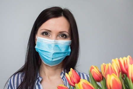 Smiling woman doctor nurse with protective medical mask, with bouquet of tulip flowers, gift, celebration, medical worker day. Mothers day. Light grey background, copy spaceの写真素材