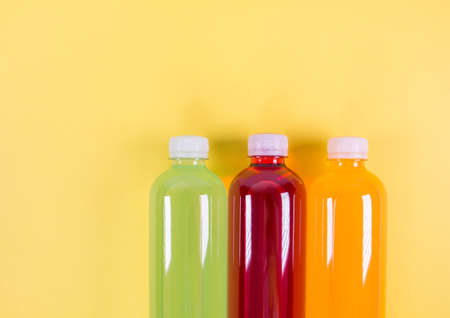 Bottles of orange, green, red smoothie on yellow background. Top view. Detox summer drink. Healthy fresh juice bottle. Vegan and vegetarian concept.の写真素材