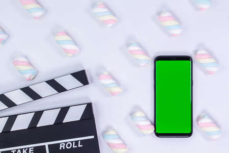 Phone mockup. Movie clapperboard and black smartphone with blank screen. White background with twisted marshmallow pattern.の写真素材
