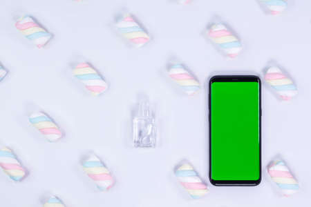 Phone mockup. Sanitizer bottle and black smartphone with blank screen. White background with twisted marshmallow pattern.の写真素材