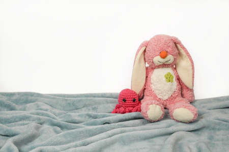 A plush bunny toy sitting on plush blanket and white wall. Plush pink bunny toy with pink knitted octopus.の写真素材