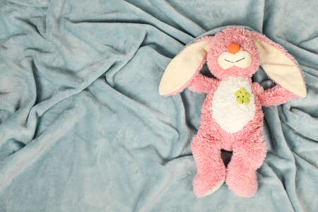 A plush bunny toy sitting on plush blanket and white wall. Plush pink bunny toy with pink knitted octopus.の写真素材