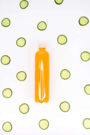 Bottle of orange smoothie on white background cucumber pattern. Top view. Detox summer drink. Healthy fresh juice bottle. Vegan and vegetarian concept.の写真素材