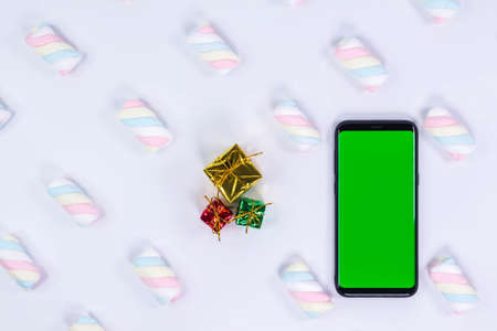 Phone mobile telephone with a vertical green screen. White background with twisted marshmallow pattern. Chroma key smartphone technology.の写真素材