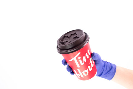 Nurse hand in medical glove holding a Tim Hortons Large Cup of Coffee. Red Tims coffee cup. Space for textのeditorial素材