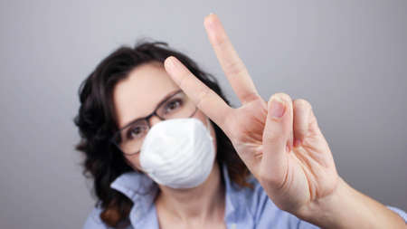 Young caucasian woman wearing face mask standing against gray wall showing and pointing up with fingers number two while smiling confident and happy. Peace sign.の写真素材